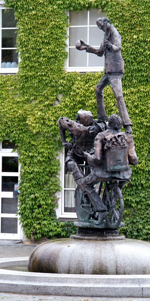 Eine Bronzestatue von Radfahrern über die ein Mann mit einem Stein in der Hand läuft.