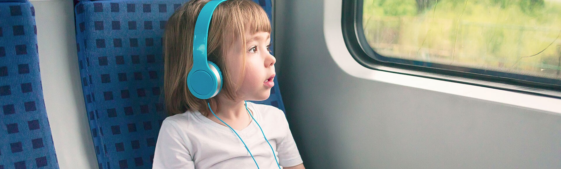 Ein kleines Mädchen sitzt mit Kopfhörern am Fensterplatz in der Bahn.