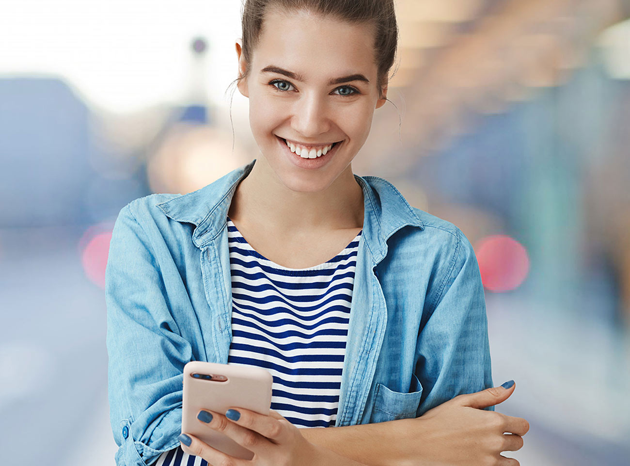 Eine junge Frau lächelt, während sie ihr Handy in der Hand hält.